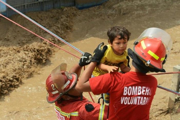Residents of the Huachipa populous district, east of Lima, are helped on March 17, 2017, by police and firemen rescue teams to cross over flash floods hitting their neighbourhood and isolating its residents