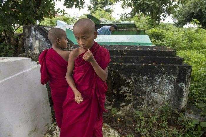 Cemetery personnel bury the body of a three-year-old child, one of three victims of an exorcism ritual in Twante, south of Yangon on October 22, 2016, as young novice monks looks on