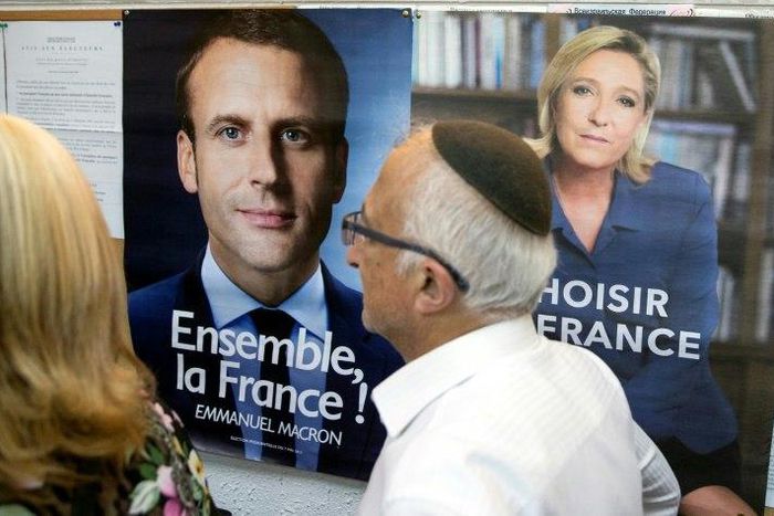 A French citizen walks past election posters of French presidential candidates Emmanuel Macron and Marine Le Pen before casting his vote at the French consulate in Tel Aviv on May 7, 2017