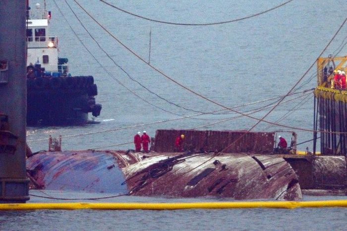 Workers check the hull of the Sewol ferry between two the barges that hauled it to the surface, nearly three years after it sank with the loss over 304 lives