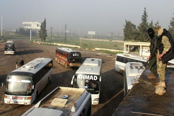 Syrian opposition fighters stand on top of a vehicle in rebel-held Rashidin, west of Aleppo city, as buses carrying people from government-held Fuaa and Kafraya arrive as part of an evacuation deal