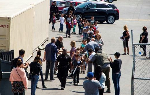A police officer leads children to be reunited with parents after a gunman entered a classroom and killed one woman and one student, before turning the gun on himself, at North Park Elementary School in San Bernardino, California