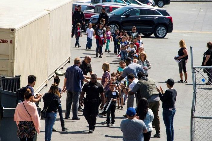 A police officer leads children to be reunited with parents after a gunman entered a classroom and killed one woman and one student, before turning the gun on himself, at North Park Elementary School in San Bernardino, California