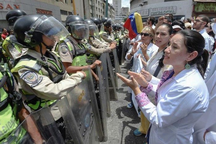 Doctors chant slogans in front of a line of National Guard personnel in riot gear during a demonstration against the shortage in medicines and in rejection of the government of President Nicolas Maduro, in Caracas on May 17, 2017