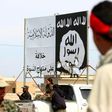 Members of the US-backed Syrian Democratic Forces stand under an Islamic State group banner in the recently recaptured town of Al-Karamah, near the IS bastion of Raqa