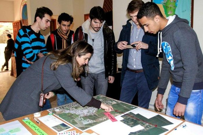 Claudia Martinez, a humanitarian worker at Burj al-Shamali refugee camp, looks at aerial shots taken by Palestinian refugees Mustafa Dakhlool (R) and Firas Ismail (L)