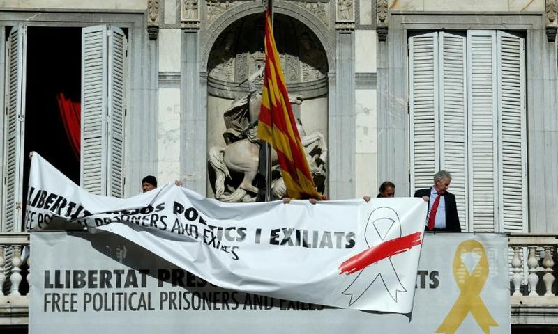 A banner reading "Free political prisoners and those exiled" bearing a white ribbon with a red brush stroke replaces an older one bearing a yellow ribbon on the balcony of the regional government's headquarters in Barcelona