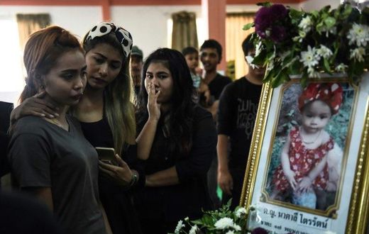 Jiranuch Trirat (L) is comforted by friends as she looks at a photograph of her 11-month-old daughter Natalie during funeral rites at a temple in Phuket, Thailand