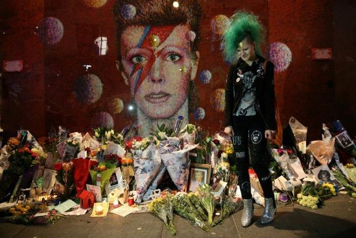 A fan poses in front of the mural of late British pop icon David Bowie created by Australian street artist James Cochran, as fans payed their respects in Brixton, south London on January 10, 2017, on the first anniversary of Bowie's death