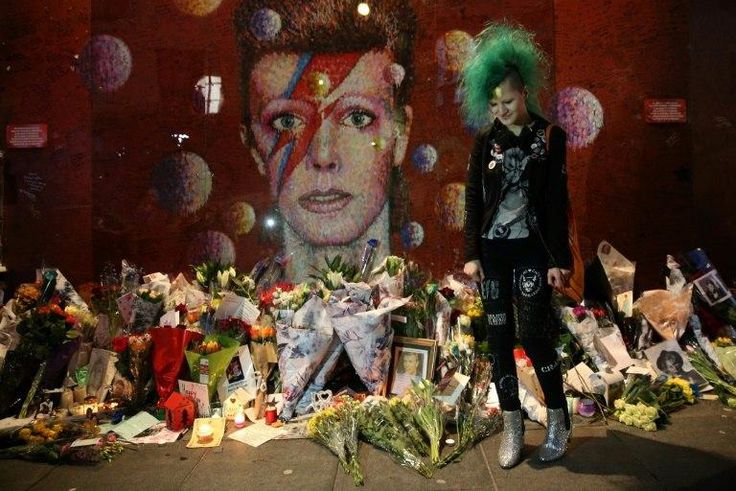A fan poses in front of the mural of late British pop icon David Bowie created by Australian street artist James Cochran, as fans payed their respects in Brixton, south London on January 10, 2017, on the first anniversary of Bowie's death