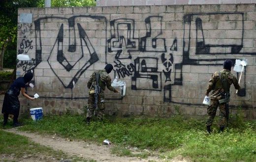 Police officers and soldiers paint over graffiti associated with the Mara Salvatrucha gang in Quezaltepeque, El Salvador