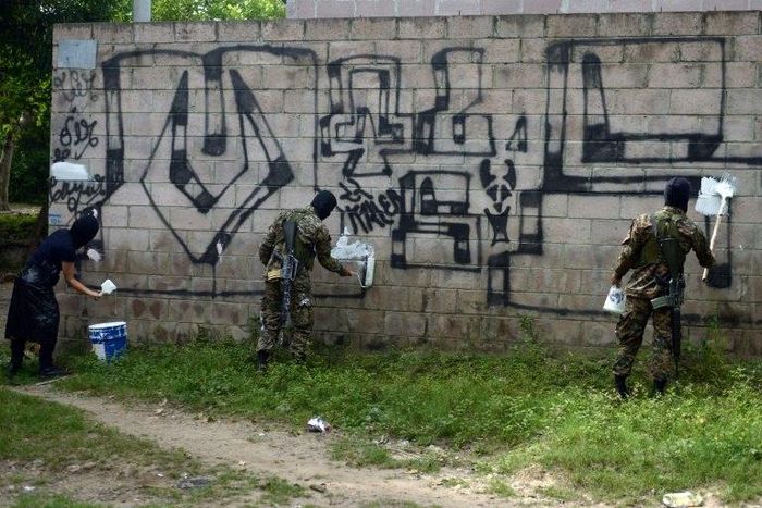 Police officers and soldiers paint over graffiti associated with the Mara Salvatrucha gang in Quezaltepeque, El Salvador