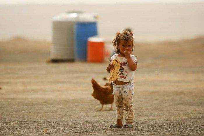 A displaced child, who fled from the Islamic State group bastion of Raqa, stands outside as she eats a loaf of bread in a camp for displaced near the town of Al-Karamah, 26 kilometres from Raqa, on May 10, 2017