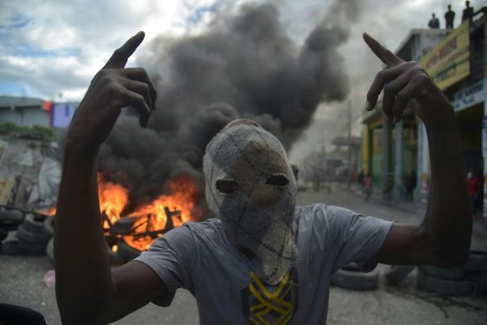 A masked demonstrator gestures before burning tires during protests in Port-au-Prince, on February 10, 2019