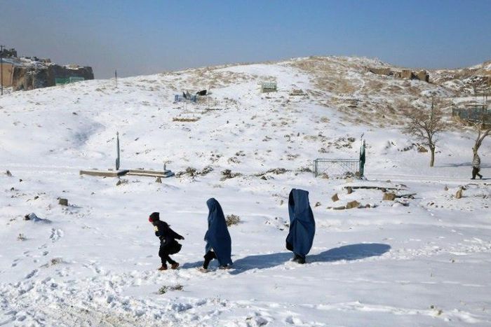 Burqa-clad women walk with a child through the snow in Ghazni province, southern Afghanistan on January 16, 2017