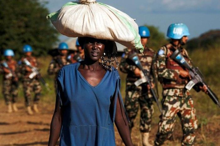 A displaced woman carries goods as UN peacekeepers patrol outside UN Protection of Civilians premises in Juba