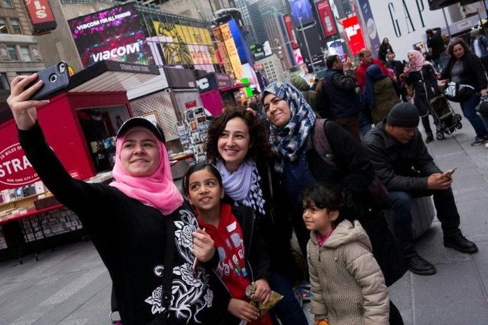 Syrian and Iraqi refugee families take selfies in Times Square during a tour of Manhattan in New York
