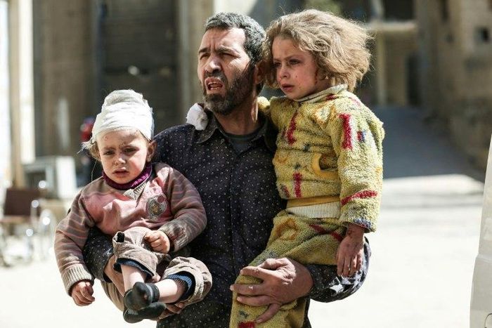 A Syrian man carries two injured children after a reported air strike in the rebel-controlled town of Hammuriyeh, on the outskirts of the capital Damascus, on March 25, 2017