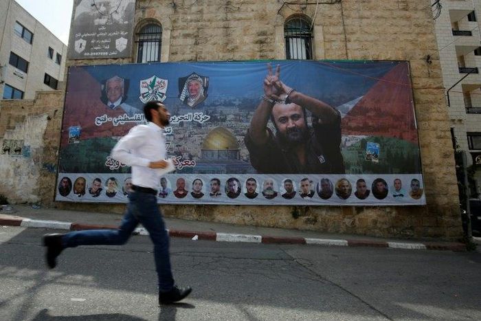 File picture of a man running past a poster of Palestinian hunger-striker and prominent prisoner Marwan Barghouti in the West Bank city of Ramallah on May 3, 2017