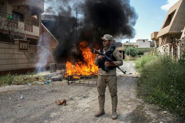 A militiaman stands guard as a family returning to Iraq's main Christian town Qaraqosh following its recapture from the Islamic State group makes a bonfire on May 5, 2017 of damaged furniture and rubbish that the jihadists left behind