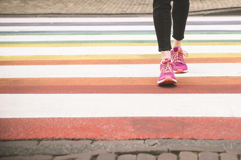 Woman crossing multi coloured zebra crossing, partial view