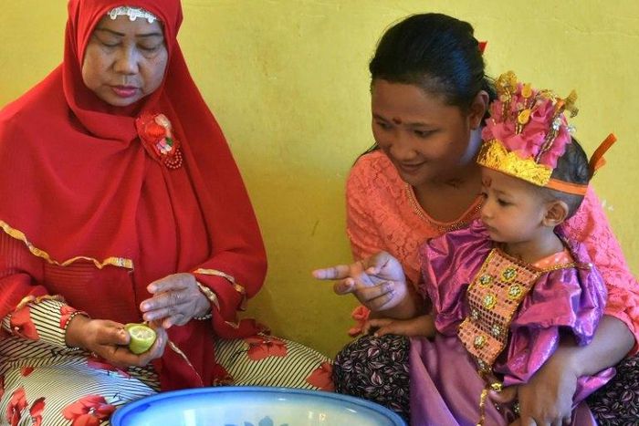 Toddler Salsa Djafar sits on her mother's lap during a circumcision ceremony in Gorontalo, Indonesia, led by a traditional healer