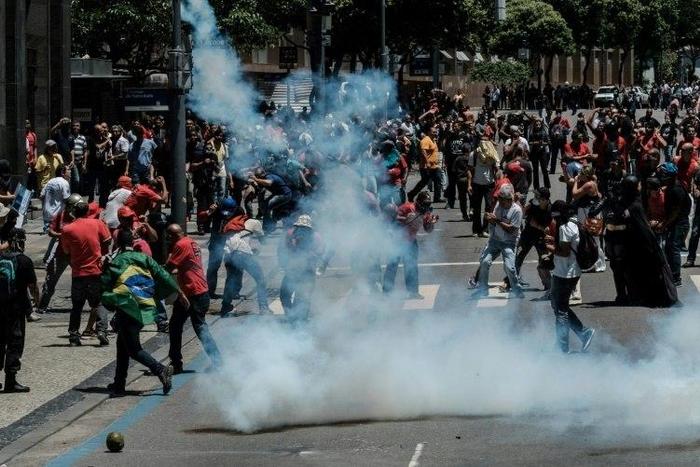 Protesters run away from tear gas during clashes with riot police following a public servants protest against austerity measures in front of the Rio de Janeiro state assembly on December 6, 2016