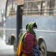 A woman covers her face with a mask as she walks along a dusty road in Kathmandu