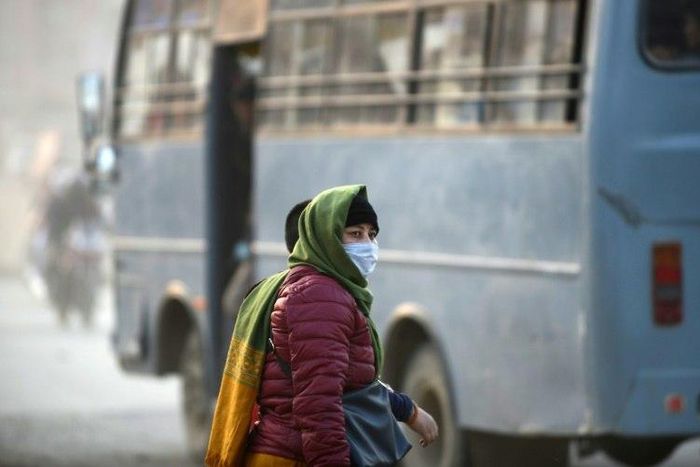 A woman covers her face with a mask as she walks along a dusty road in Kathmandu
