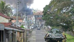 A Philippine Marines truck and armoured personnel carrier speed away as black smoke billows from burning houses after military helicopters fired rockets at militant positions in Marawi on the southern island of Mindanao