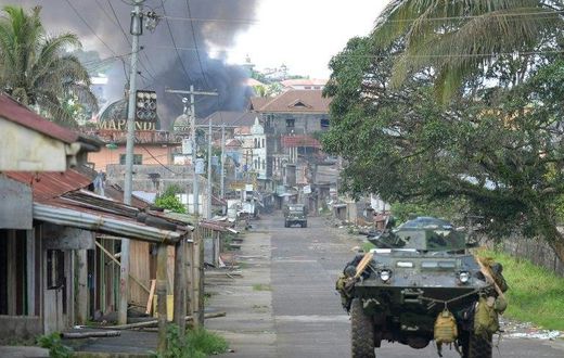 A Philippine Marines truck and armoured personnel carrier speed away as black smoke billows from burning houses after military helicopters fired rockets at militant positions in Marawi on the southern island of Mindanao
