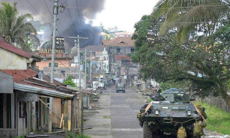 A Philippine Marines truck and armoured personnel carrier speed away as black smoke billows from burning houses after military helicopters fired rockets at militant positions in Marawi on the southern island of Mindanao