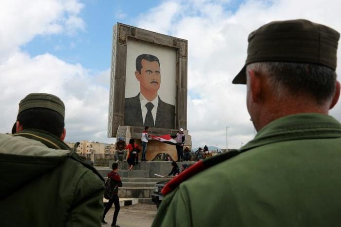 Protesters hold a national flag under a portrait of Syrian President Bashar al-Assad in the Syrian Golan Heights, during a demonstration on March 26, 2019