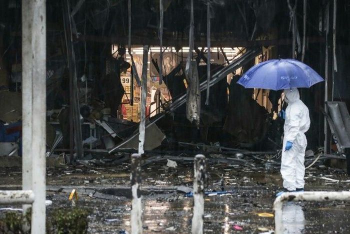 A Thai forensics worker shields himself with an umbrella whilst inspecting the aftermath of a bomb attack in the town centre of Pattani on May 9, 2017