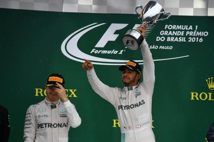 Mercedes driver Lewis Hamilton celebrates with the trophy after winning the Brazilian Grand Prix ahead of title rival and Mercedes teammate Nico Rosberg (L) on November 13, 2016