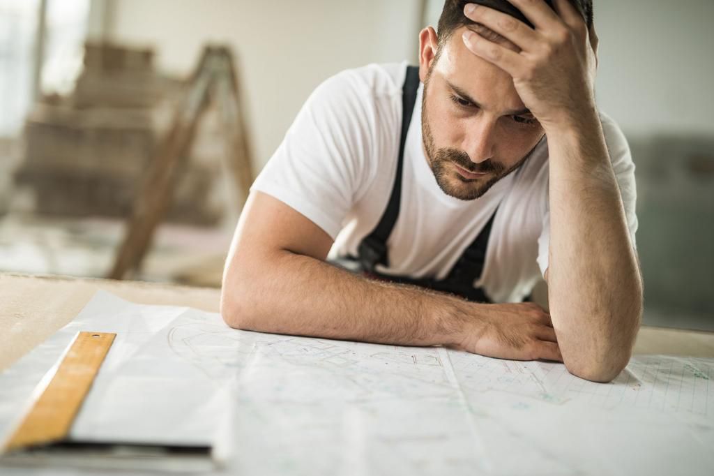 Frustrated manual worker having problems with blueprints at construction site.
