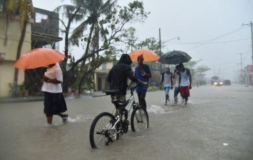 Haitian people travel in a flooded street through the rain, during a tropical storm in the commune of Les Cayes, Haiti, on October 21, 2016
