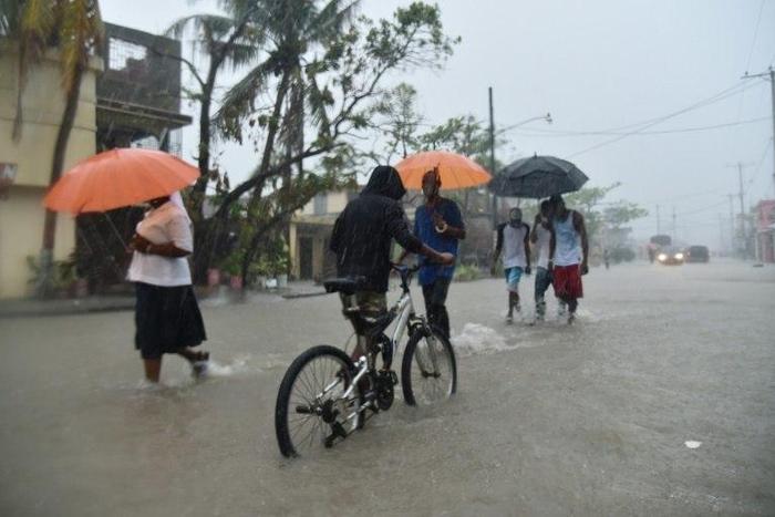 Haitian people travel in a flooded street through the rain, during a tropical storm in the commune of Les Cayes, Haiti, on October 21, 2016