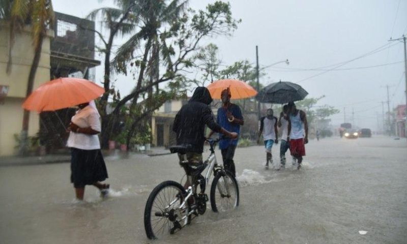 Haitian people travel in a flooded street through the rain, during a tropical storm in the commune of Les Cayes, Haiti, on October 21, 2016