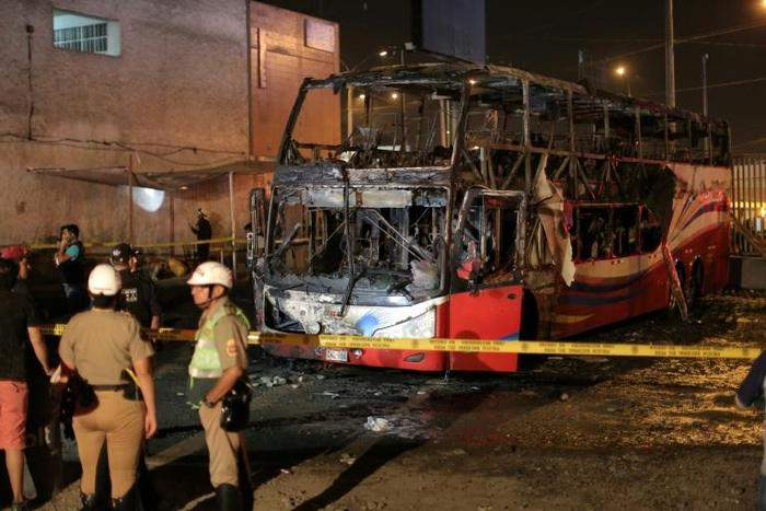 Police stand around the charred remains of a bus that caught fire in Lima killing 20 people