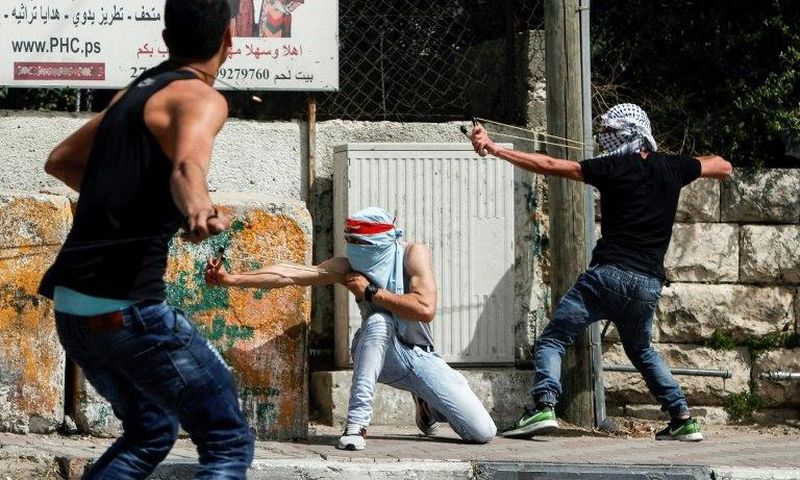 Palestinian protesters use slingshots to hurl stones towards Israeli security forces during clashes in the West Bank town of Bethlehem on April 21, 2017, in solidarity with the hunger striking prisoners