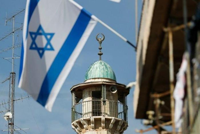 An Israeli flag is pictured in front of the minaret of a mosque in the Arab quarter of Jerusalem's Old City on November 14, 2016 Israeli Prime Minister Benjamin Netanyahu said he backed a bill limiting the volume of calls to prayer from mosques, a prop...