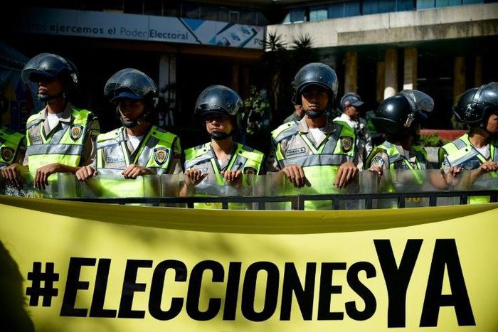 Riot police stand behind a banner that reads "Elections now" in fornt the National Electoral Council (CNE) in Caracas on January 2, 2017