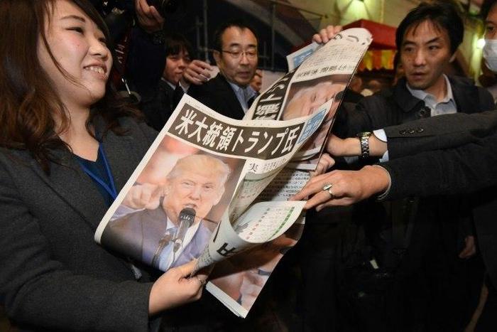 A woman in Tokyo gives out extra editions of a newpaper reporting the victory of Donald Trump in the US presidential election