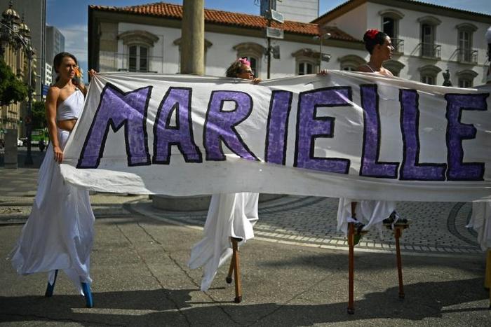 Women walk on stilts while holding a banner in memory of Rio councillor Marielle Franco, at the location in Rio de Janeiro where she was shot dead