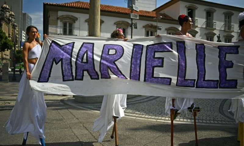 Women walk on stilts while holding a banner in memory of Rio councillor Marielle Franco, at the location in Rio de Janeiro where she was shot dead