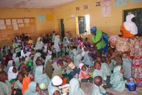 Teachers sharing food for primary school pupils sitting on the floor in an overcrowded classroom