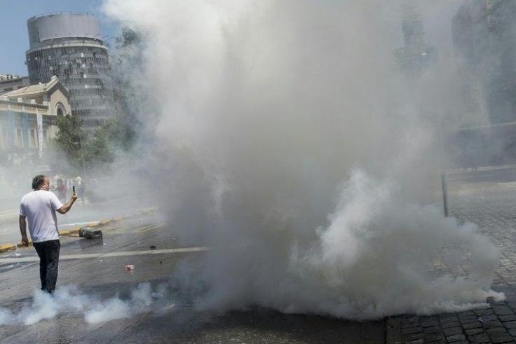 A man takes pictures as workers clash with the riot police during a protest against the Pension Fund Administrators (AFP) - Chile's privatized pension system - in front of the La Moneda presidential palace in Santiago, on November 4, 2016