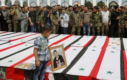 A Syrian boy places a picture on top of a coffin during a funeral ceremony at the Sayyida Zeinab shrine on the outskirts of Damascus on April 26, 2017 for victims of a bombing targeting evacuees from besieged government-held towns