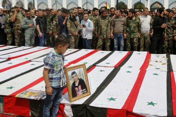 A Syrian boy places a picture on top of a coffin during a funeral ceremony at the Sayyida Zeinab shrine on the outskirts of Damascus on April 26, 2017 for victims of a bombing targeting evacuees from besieged government-held towns